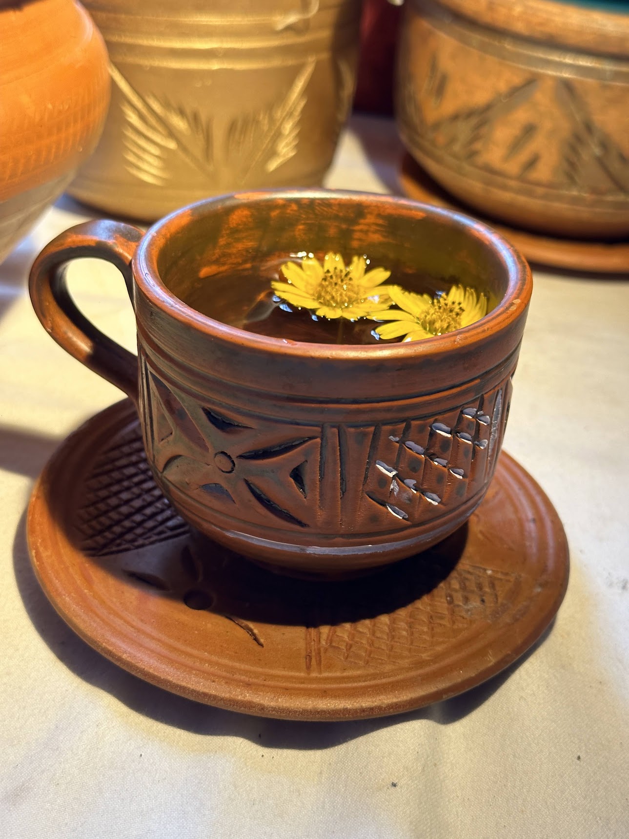 Intricately etched terracotta tea cup with yellow blossoms floating in tea under warm sunlight